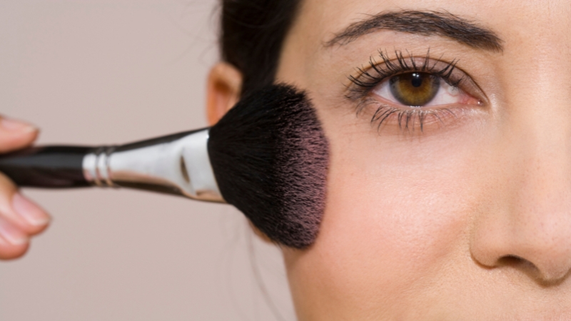 A makeup brush applies color to the cheek in a close-up shot showing how to apply blush for your skin tone